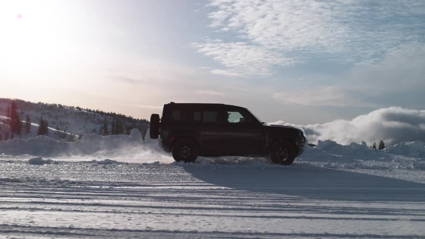 A sport utility vehicle drives on a snowy road in slow motion with trees scattered in the background and snow everywhere