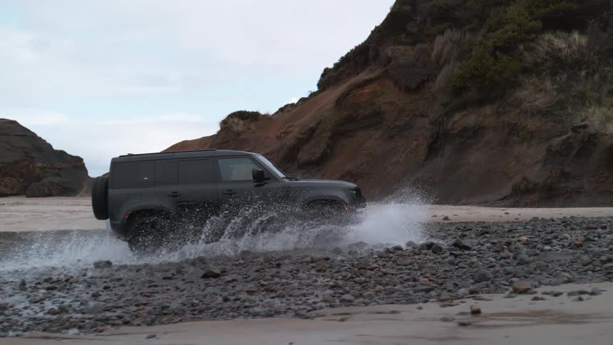 Black land rover defender drives on beach