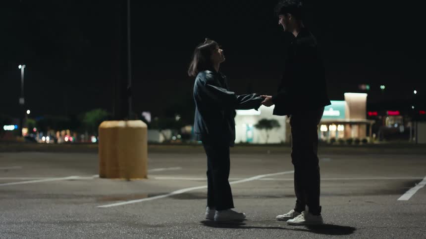 Man and woman cuddle and hold hands at the parking lot at night