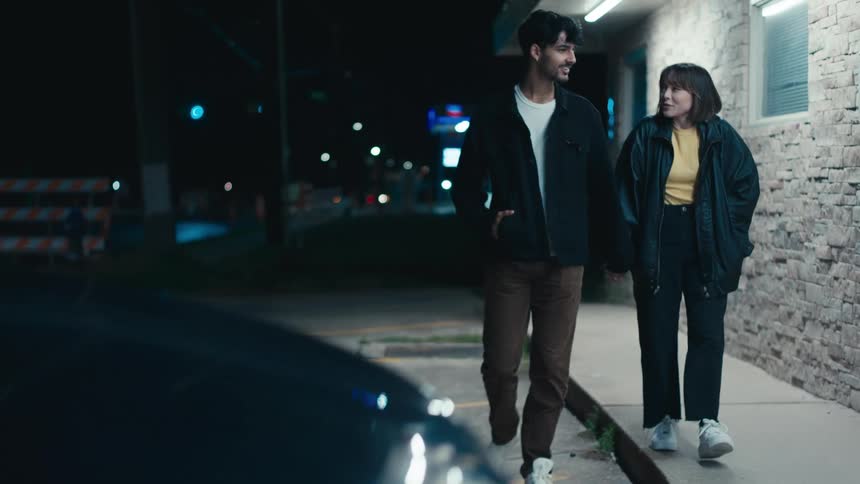 Couple holding hands walks next to building at night