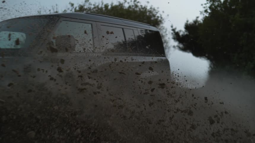 A vehicle splashes up mud while it drives through a puddle