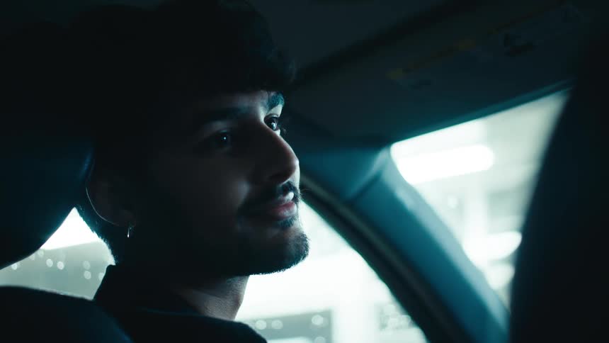 A man in a car seat with his head leaning into the headrest smiles and nods as he speaks to someone in the seat beside him
