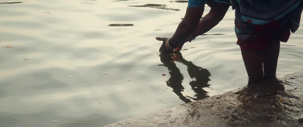 A woman places a recipient with a lit candle in a body of water letting it float away
