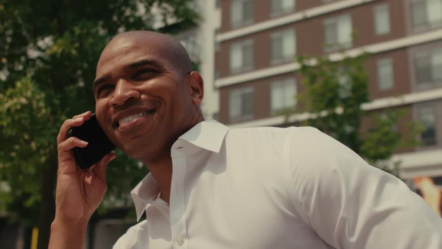A man is outside on a call on his smartphone and smiles