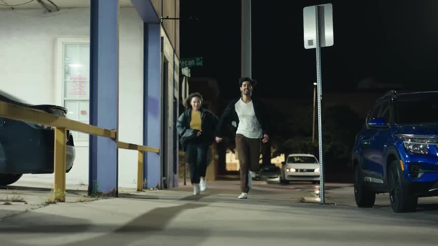 Couple holds hands while running along sidewalk at night