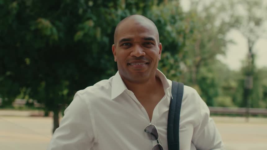 A man smiles while standing in front of a tree