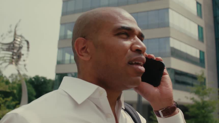 A man looks serious as he talks on his smart phone in front of a building
