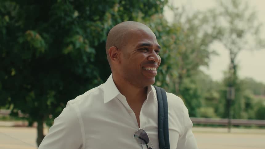 A man is standing outside in a park smiling and laughing