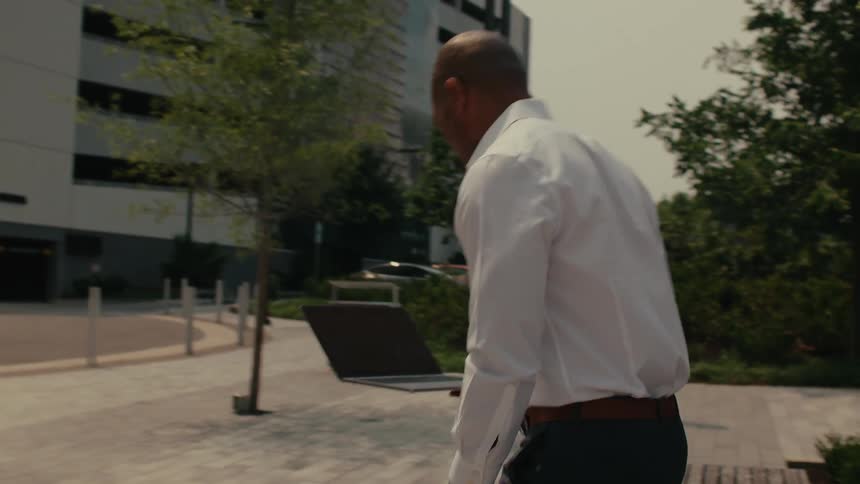 A man sits on a bench downtown with his laptop