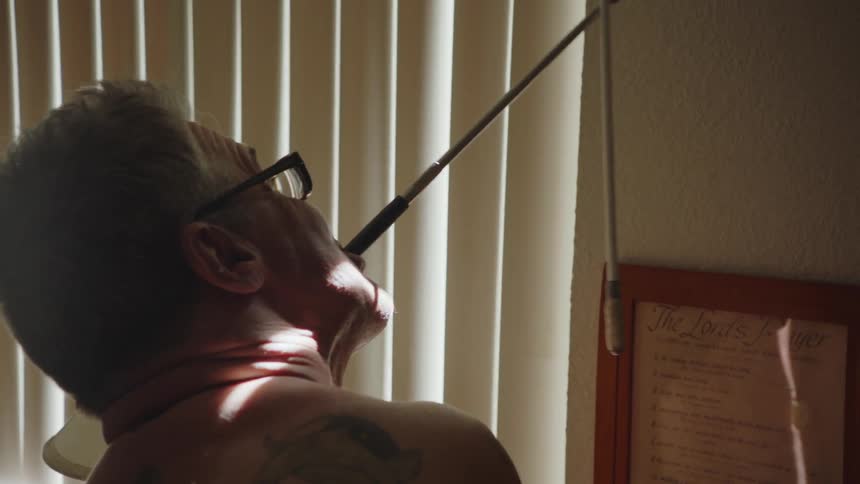 Disabled man with glasses and tattoo opens blinds with his mouth using stick
