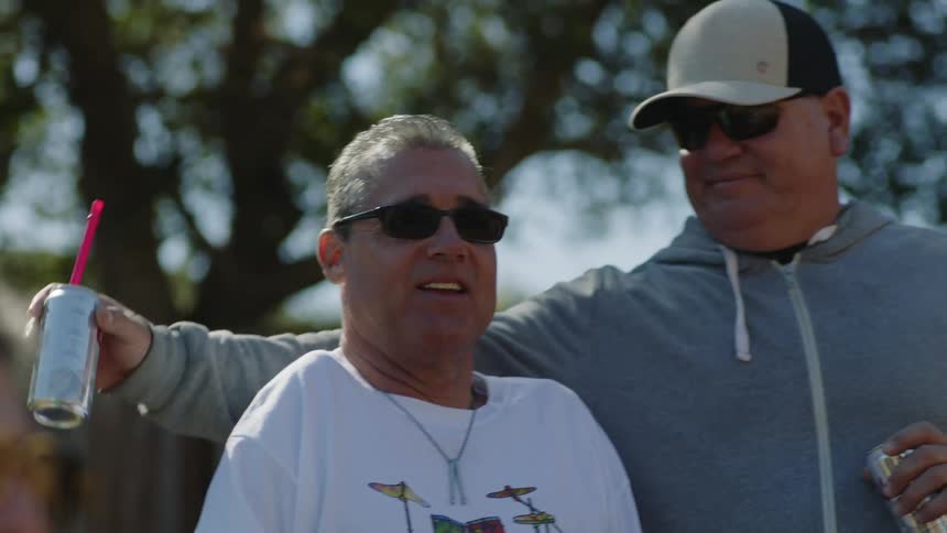 Mand wearing hat sunglasses and gray jacket holds physically disabled man in the yard