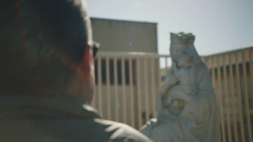 A man stares at a statue of a woman with a crown holding a baby