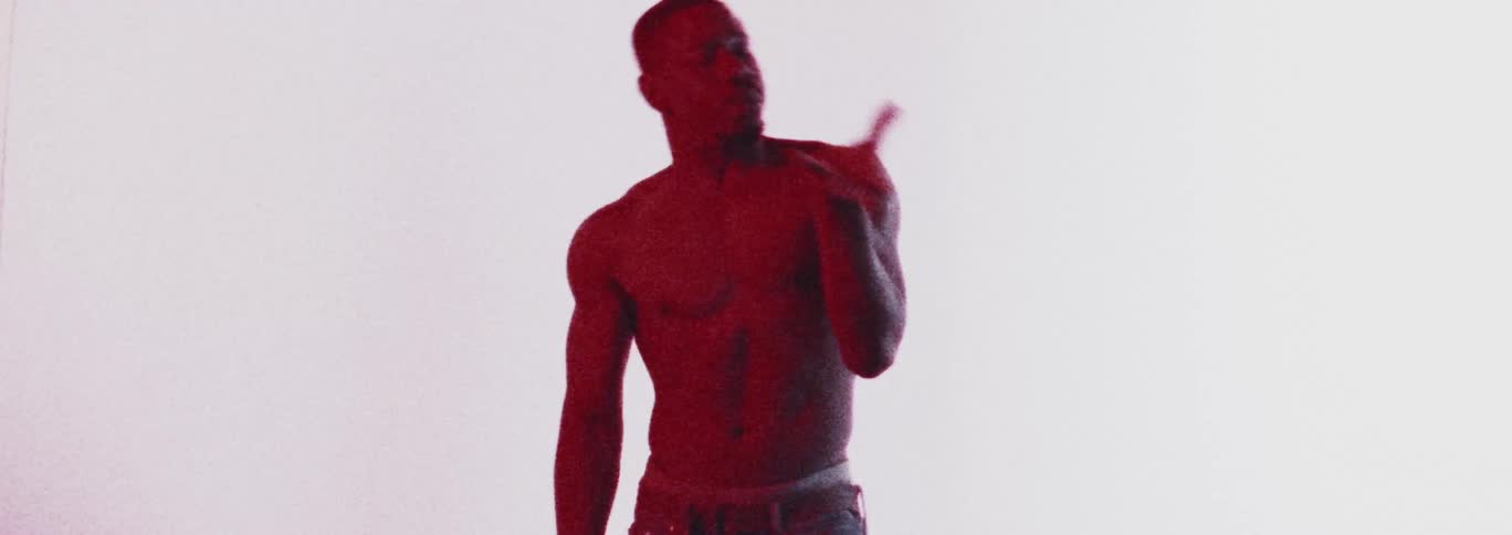 Topless man with earrings and jeans dances in red light in the studio