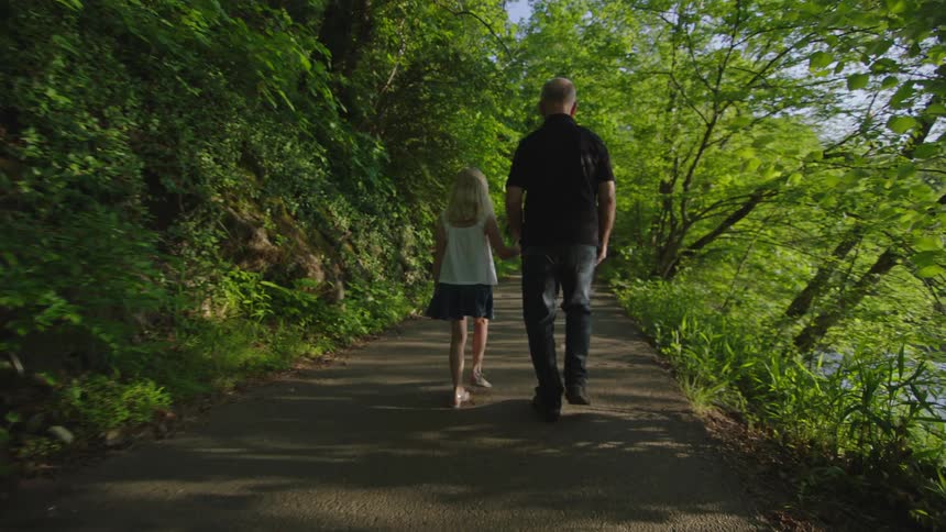 Granddaughter guides her blind grandfather down a path while he uses walking stick