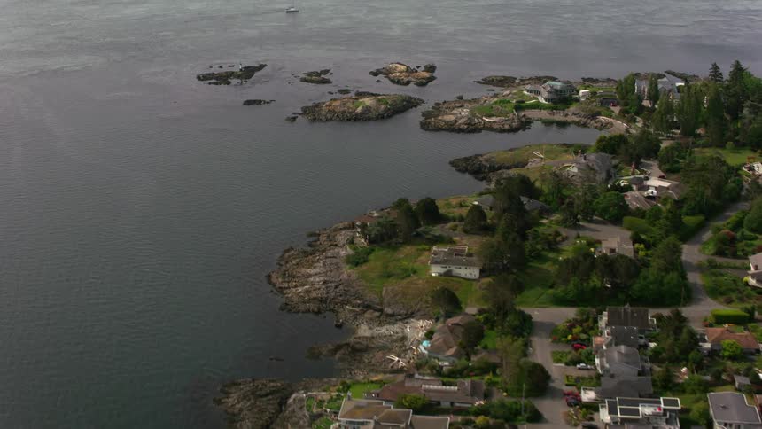 A coastal community with cars parked in driveways of houses and mansions with many trees along the peninsula