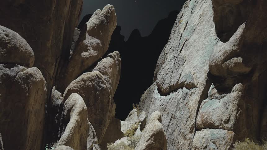 Large gray rock formation with large crevice in total blackness but with white spotlight moving across fading from black and back out again search light helicopter drone light