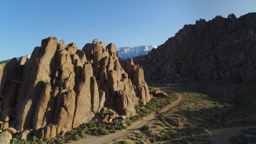 Dirt roads cut through scrubland between craggy mountains and rock outcroppings under ablue sky