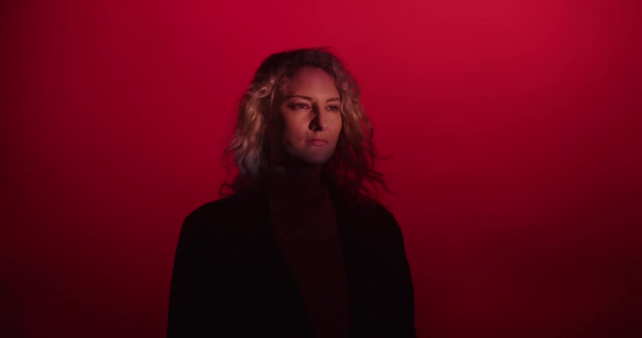 Young blonde woman face comes out of the shadows inside a dimly lit red room