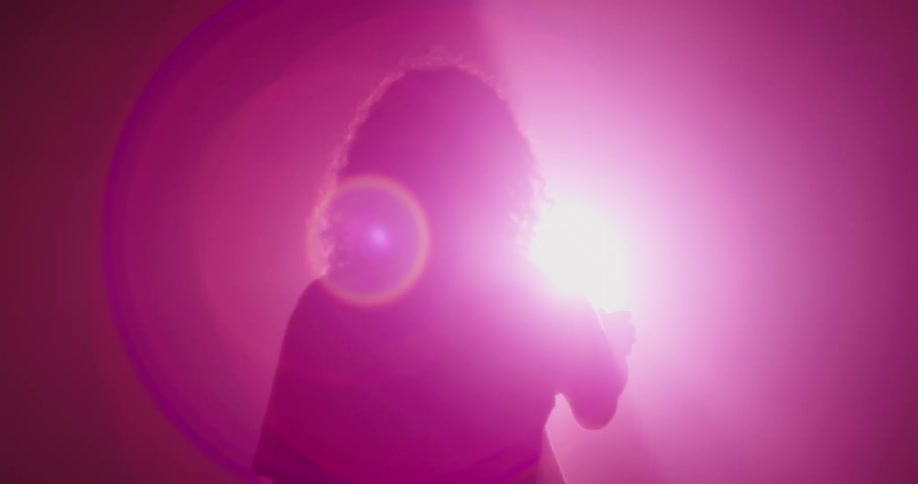 A woman in silhouette is bathed in purple light and slowly moves her hand in front of the light source