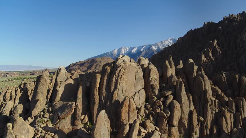 An aerial of a rocky mountain range with high peaks and shadows cast over the valley