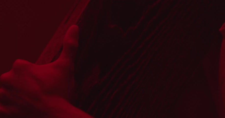 Red light shines on a mans face as he holds a piece of wood and looks up