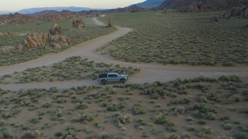 A van driving through a dirt road crossing a grassy plain surrounded by rock formations