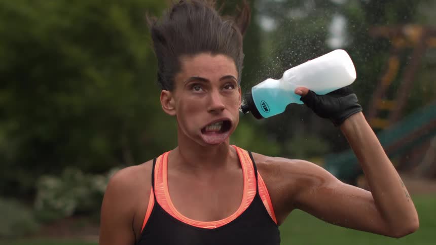 A strong wind blows causing a young woman's mouth to open and her pouring drink to spray away
