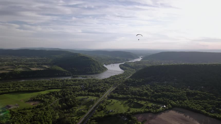 A glider flies over a river surrounded by forest