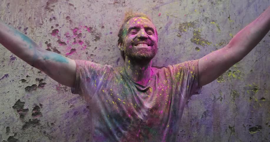 A man stands with his arms up while covered in colored powder