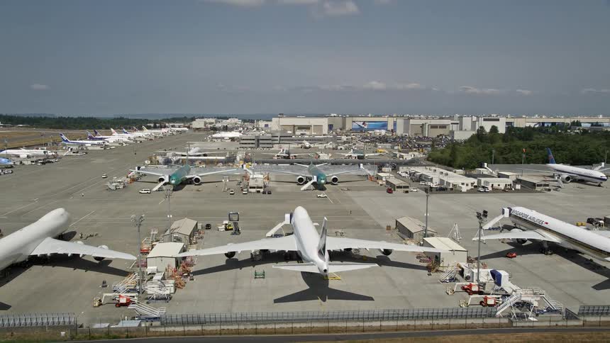 Aerial view of parked airliners and ascending jetliners approaching the Boeing Everett Factory near Paine Field on a sunny day in Washington State