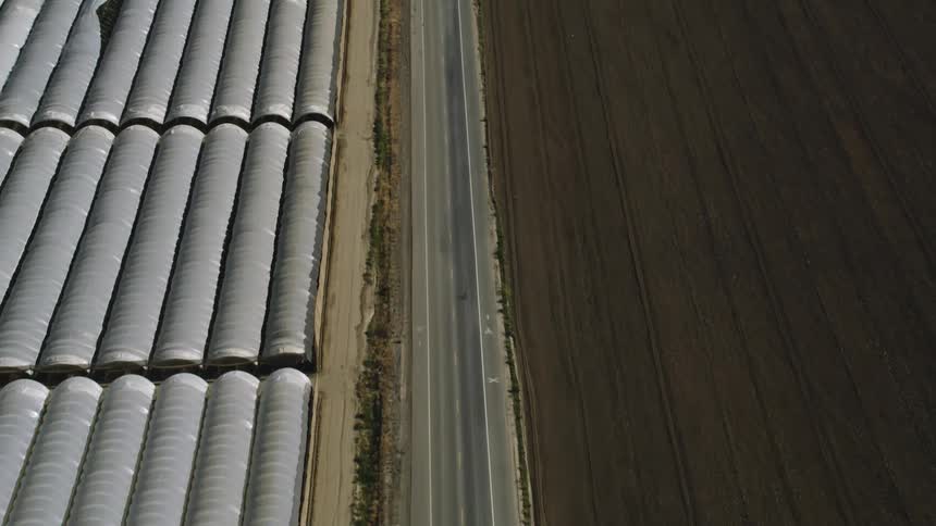 Aerial view of vehicles driving on highway between greenhouses and fields