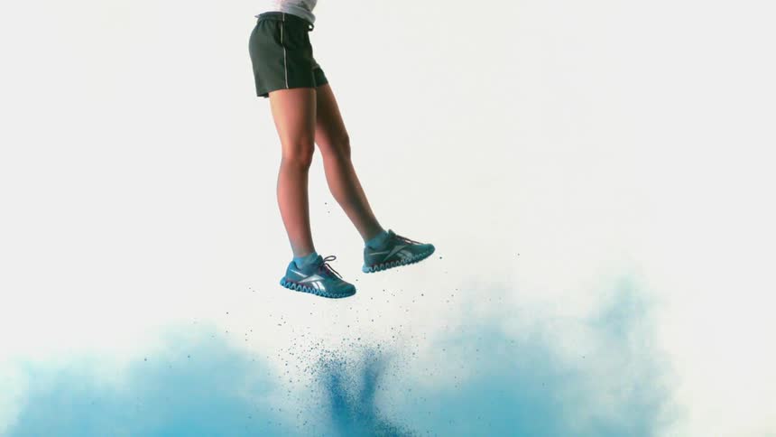 A person jumps high in the air with blue powder under them