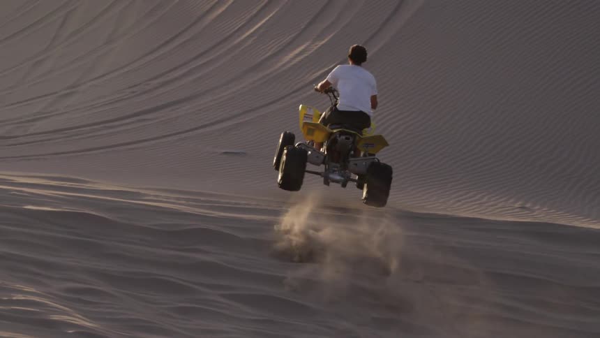 A man is riding a four wheeler around sand dunes