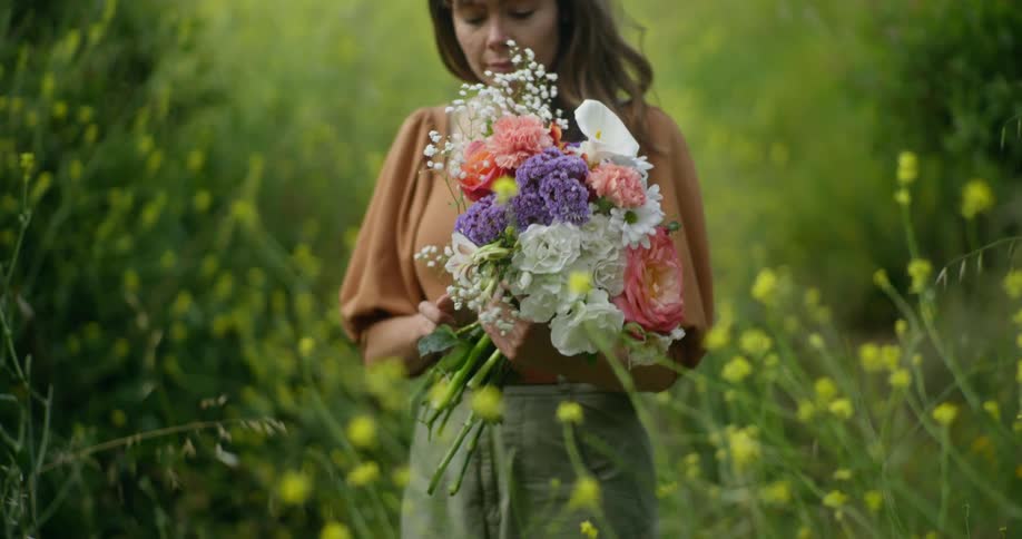 Woman stands in meadow gathering flowers into a bouquet