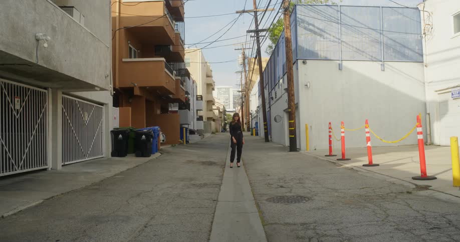 Woman stands in middle of alley between apartment buildings