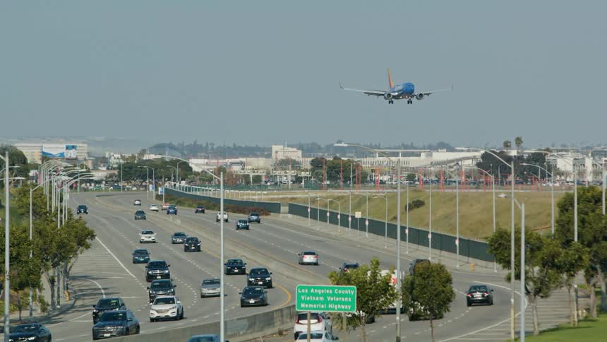 A plane is landing as traffic moves on the highway