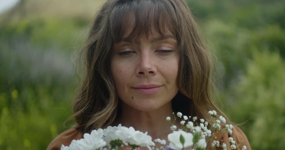 A woman is standing outside holding a bouquet of flowers as she looks up and softly smiles