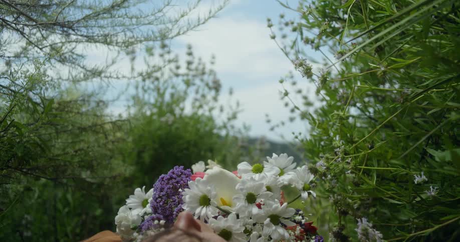 Woman lying on ground with mountains in the distance pulls bouquet to her chest