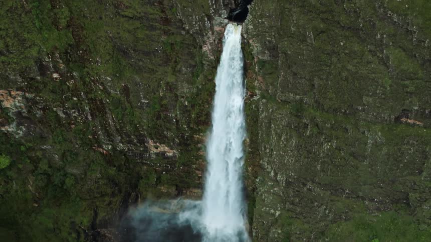An aerial of a tall gushing waterfall over a large mountain ledge
