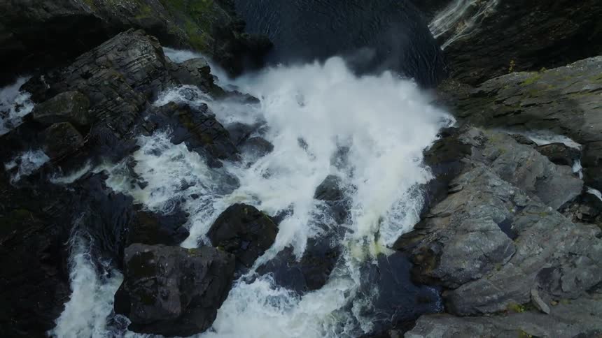 Drone view of the top of a waterfall as the water cascades over the rocky cliff