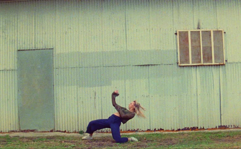 Woman dances next to corrugated metal building