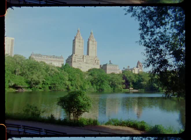 Benches sit on path across reflective water from historic midrise buildings with twin tower