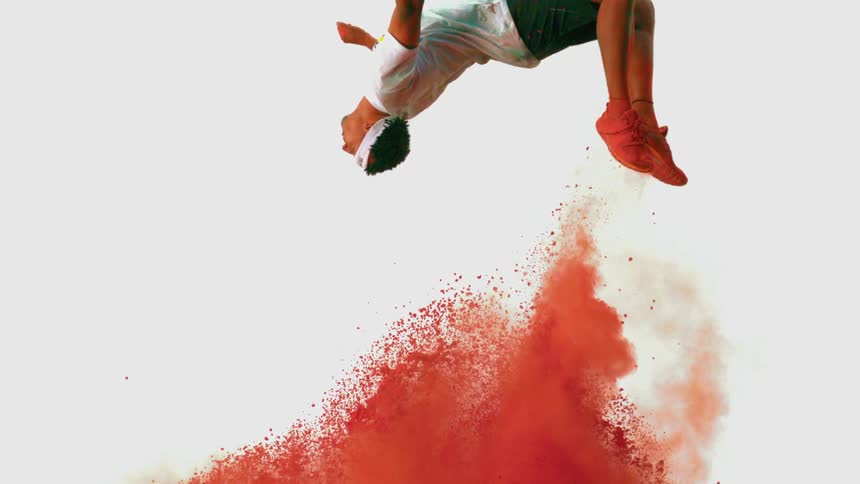 An African American man does a backflip as red powder explodes