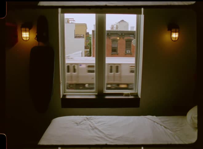 Window in bedroom shows train passing on elevated between apartment buildings