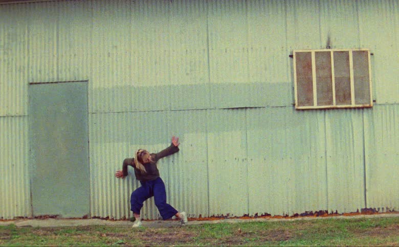 Young woman dances energetically in front of a building caught on vintage film