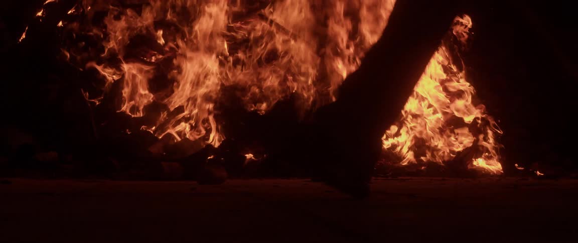 The view is of people walking outdoors by a bon fire