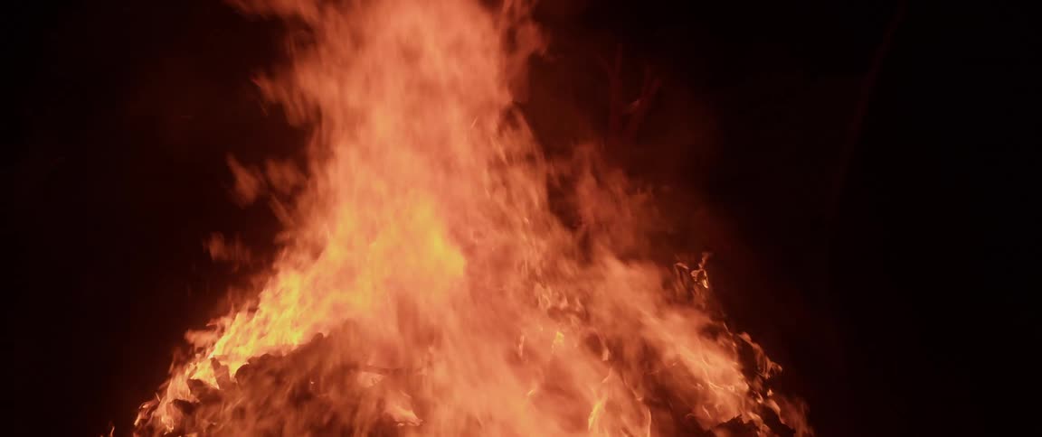 People passing by are silhouetted against bonfire