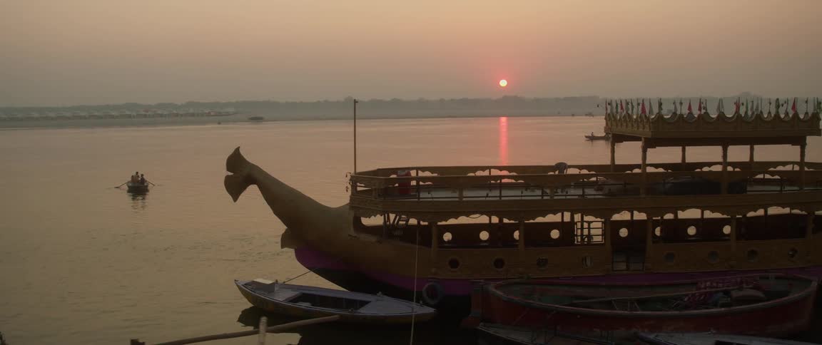 The sun setting over the water as boats are paddled across the surface by people