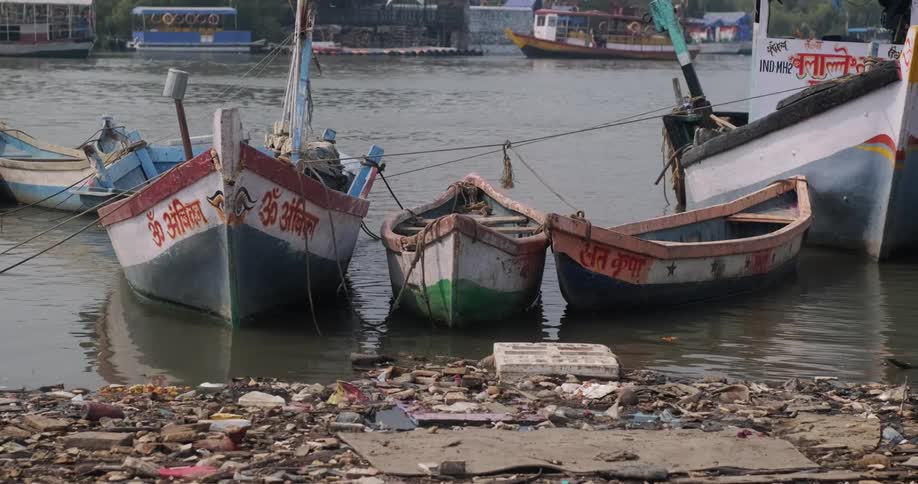 Boats anchored together on the coast near garbage piled in the water