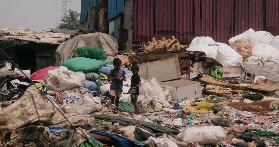 Two young boys standing together talking while on a large pile of garbge as they look at items in their hands